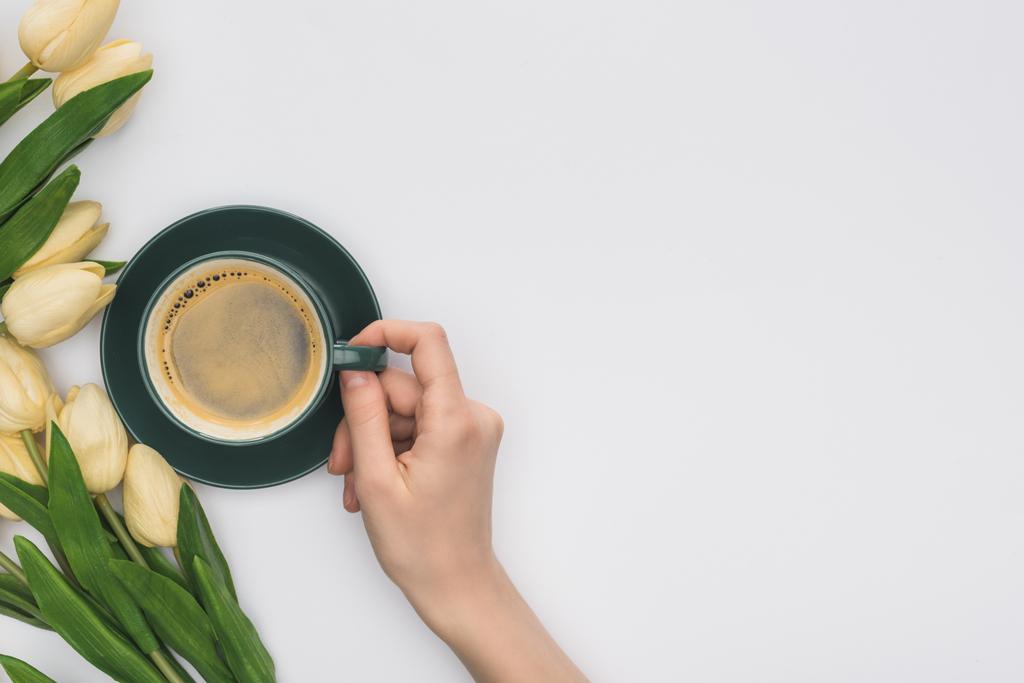 Beyaz lalelerin yanında elinde bir fincan taze kahve tutan bir kadın görüntüsü. - Fotoğraf, Görsel