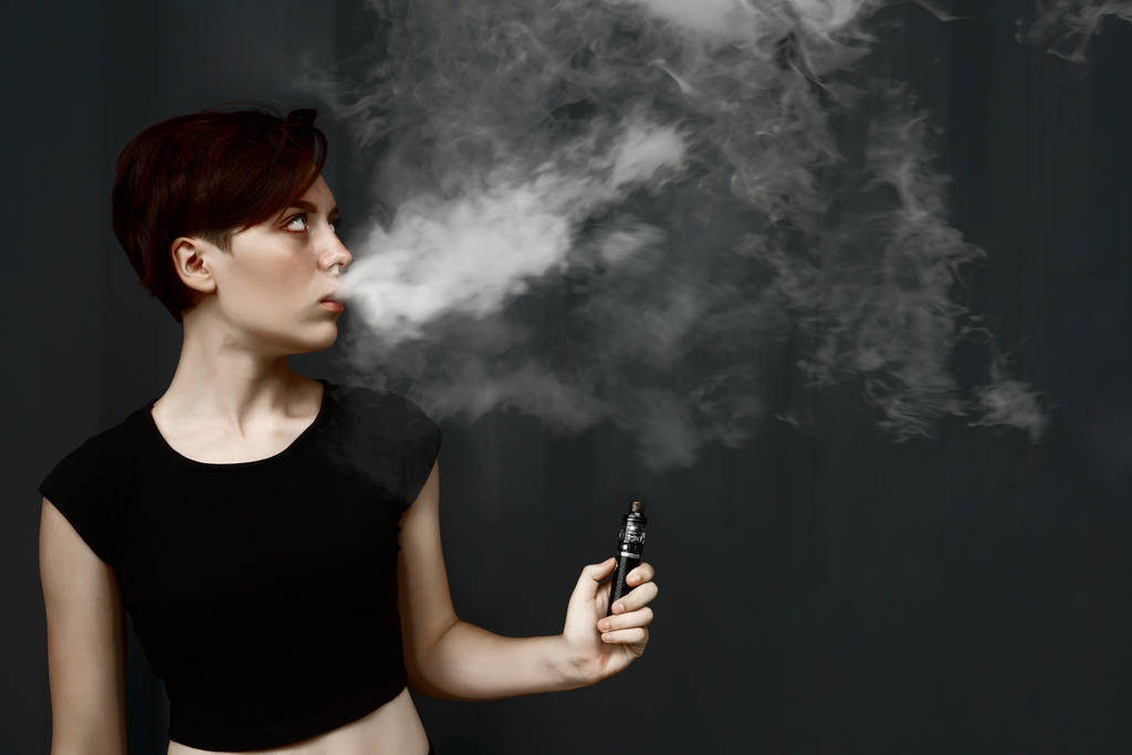 νεαρή κοπέλα καπνίζει ηλεκτρονικό τσιγάρο. θηλυκό μοντέλο που ατμίζει έναν εξατμιστήρα  - Φωτογραφία, εικόνα