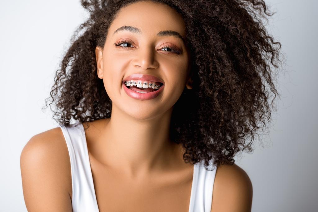 смеющаяся африканская американка с зубными скобками, изолированная от серых
 - Фото, изображение
