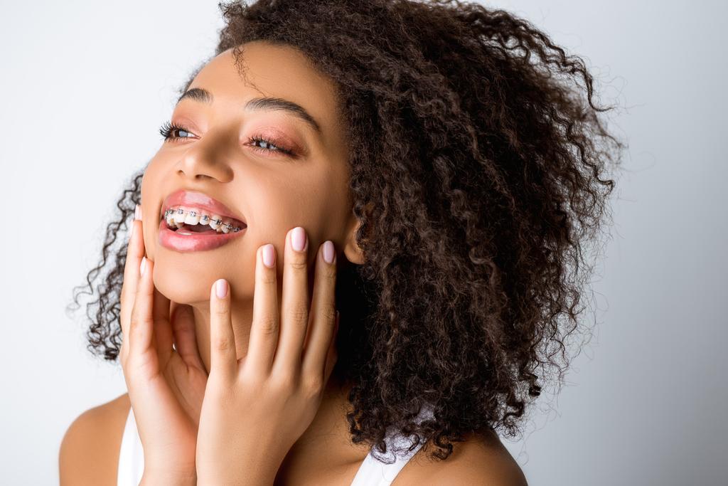 hermosa riéndose chica afroamericana con frenos dentales, aislado en gris
 - Foto, imagen