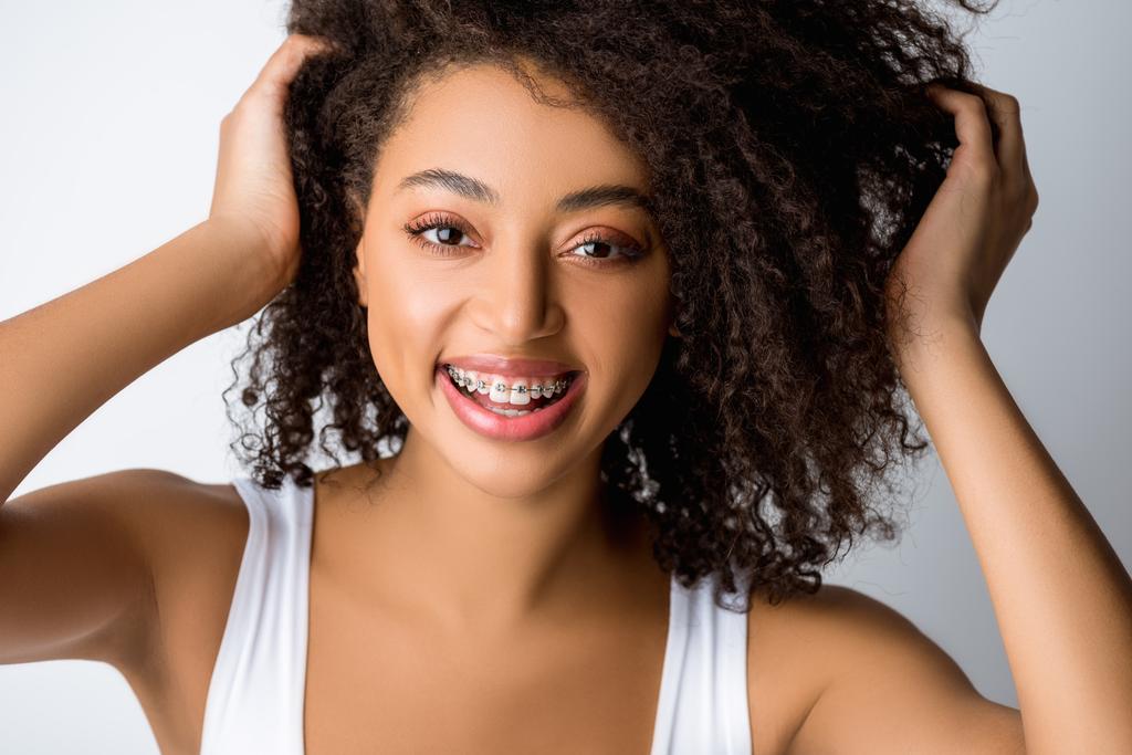beautiful positive african american girl with dental braces, isolated on grey - Photo, Image