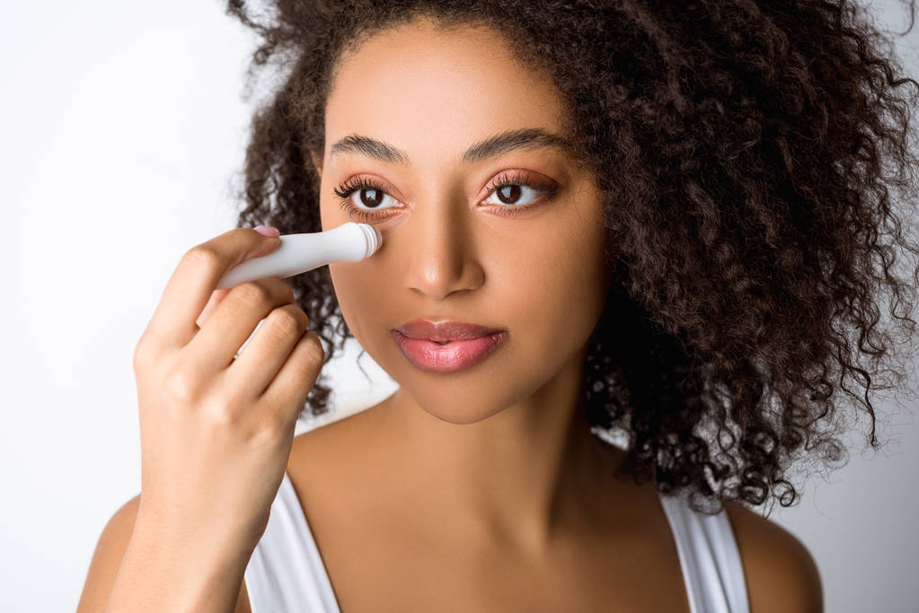 attractive african american girl using moisturizing eye roller, isolated on grey - Photo, Image