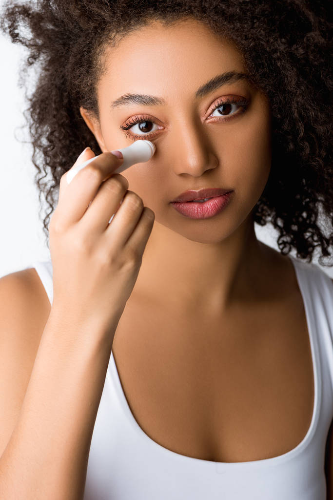 hermosa chica afroamericana usando rodillo de ojo hidratante, aislado en gris
 - Foto, Imagen