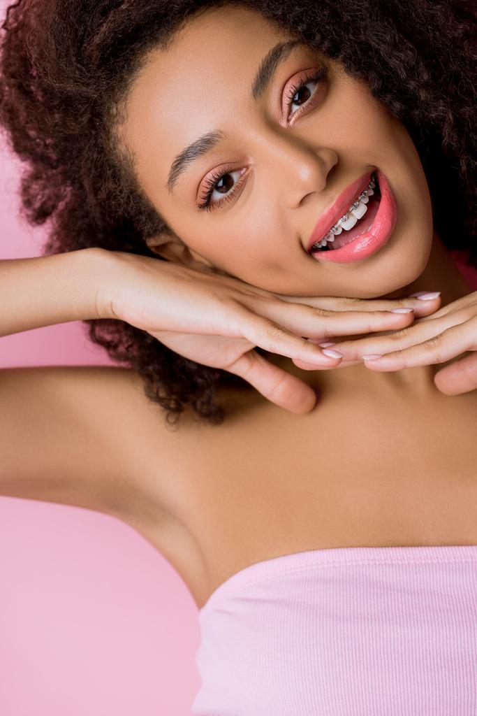 όμορφη χαμογελαστή Αφροαμερικανή με οδοντικά σιδεράκια, απομονωμένη σε ροζ - Φωτογραφία, εικόνα