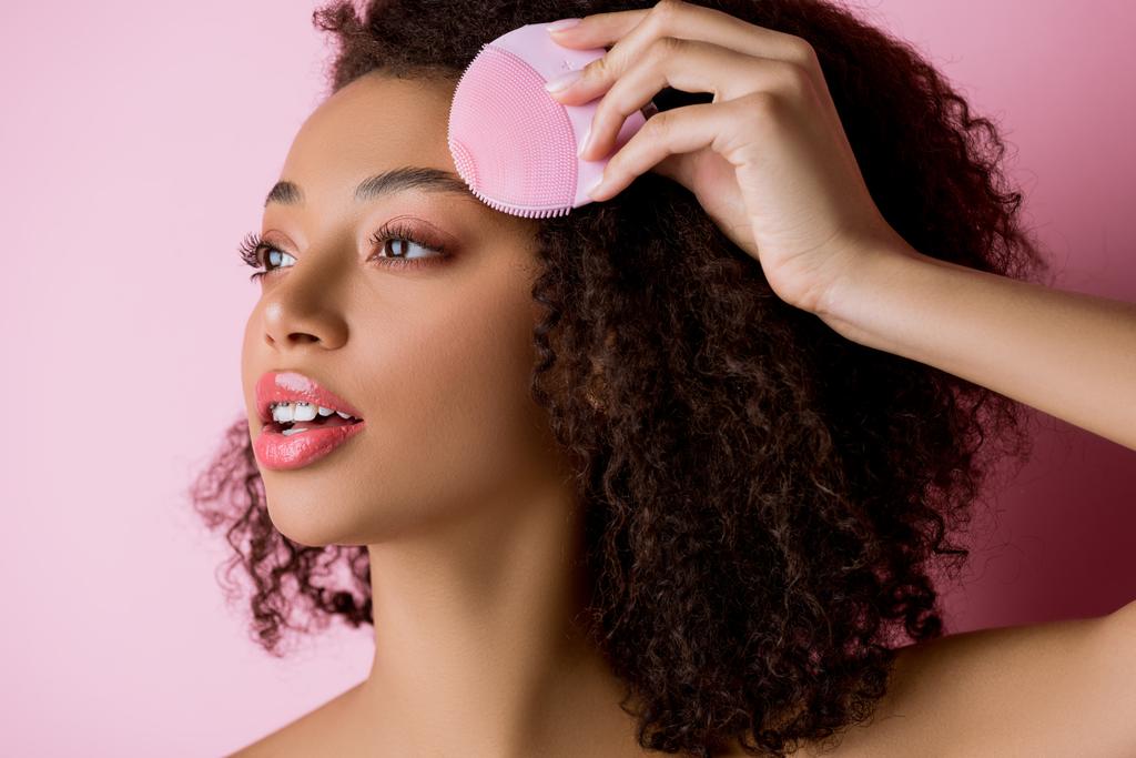 afro-américaine les yeux fermés à l'aide d'une brosse nettoyante au silicone, isolée sur rose
 - Photo, image