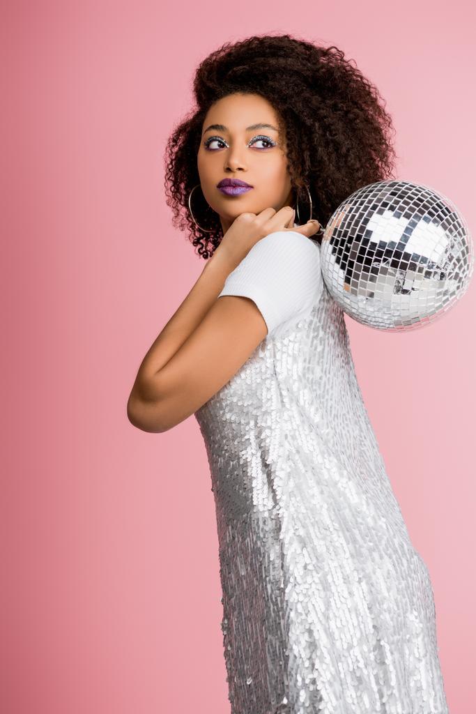 stylish african american girl in paillettes dress holding disco ball, isolated on pink - Photo, Image