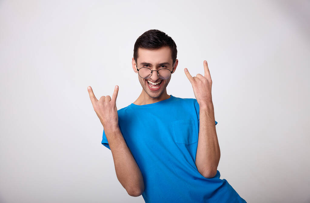 A cute young man in a blue T-shirt has fun on a white background. - Photo, Image