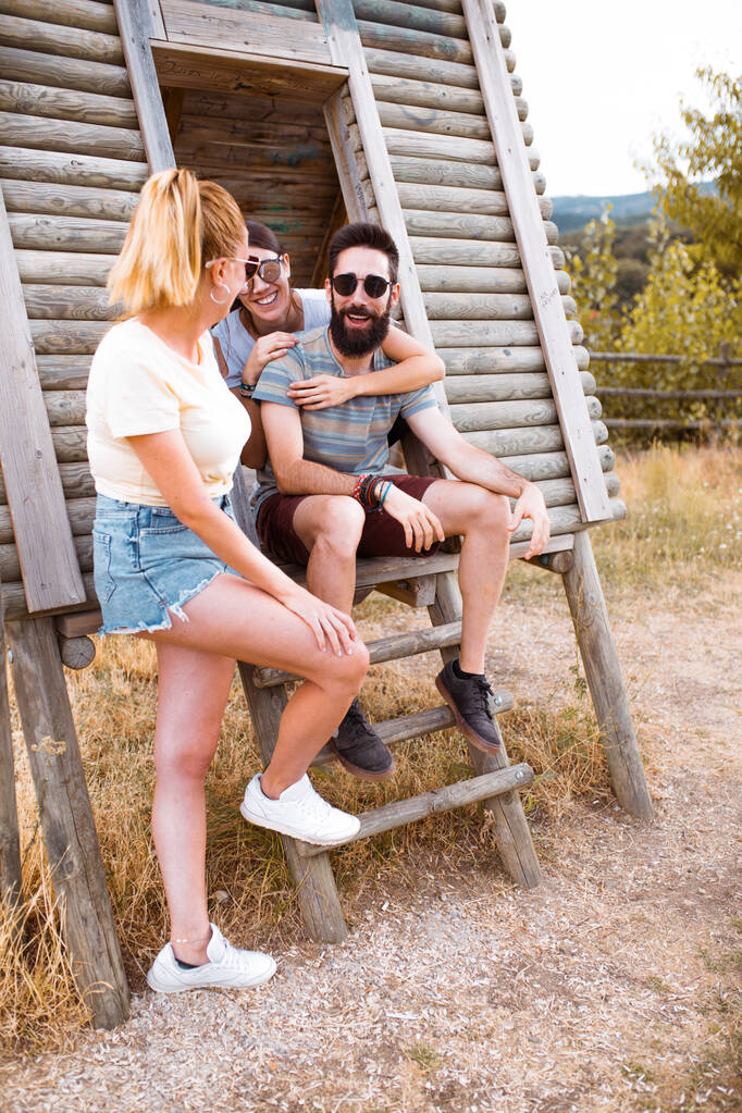 Turyści się relaksują. Grupa trzech przyjaciół siedzi na drewnianych schodach obozowych ciesząc się i śmiejąc na wsi. Przygody obozowe i koncepcja podróży. - Zdjęcie, obraz