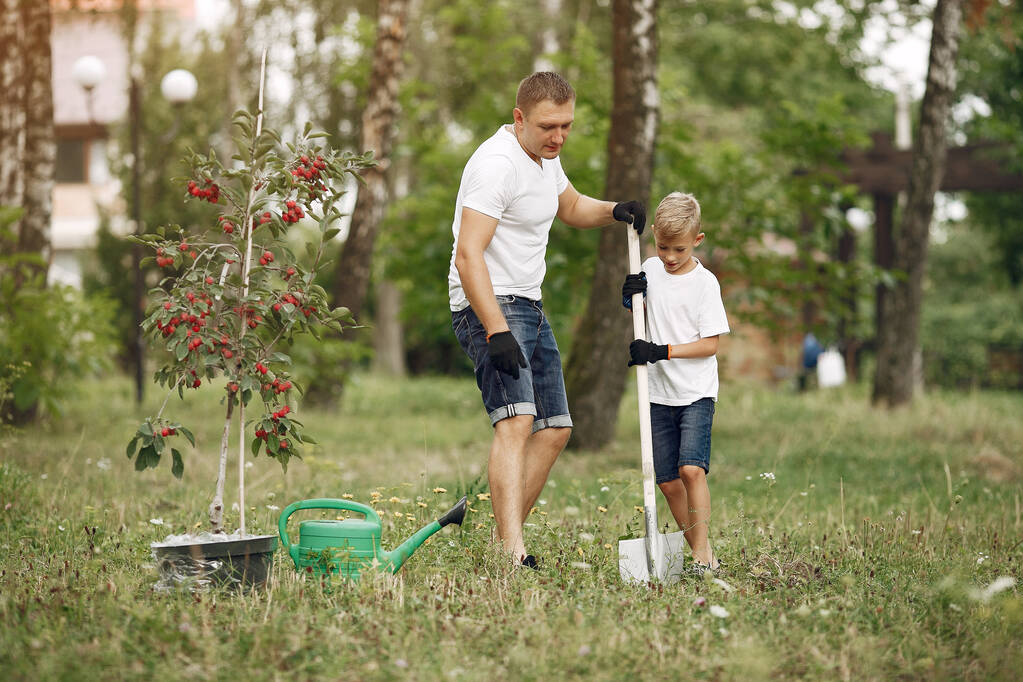 Vader met zoontje plant een boom op een erf. - Foto, afbeelding