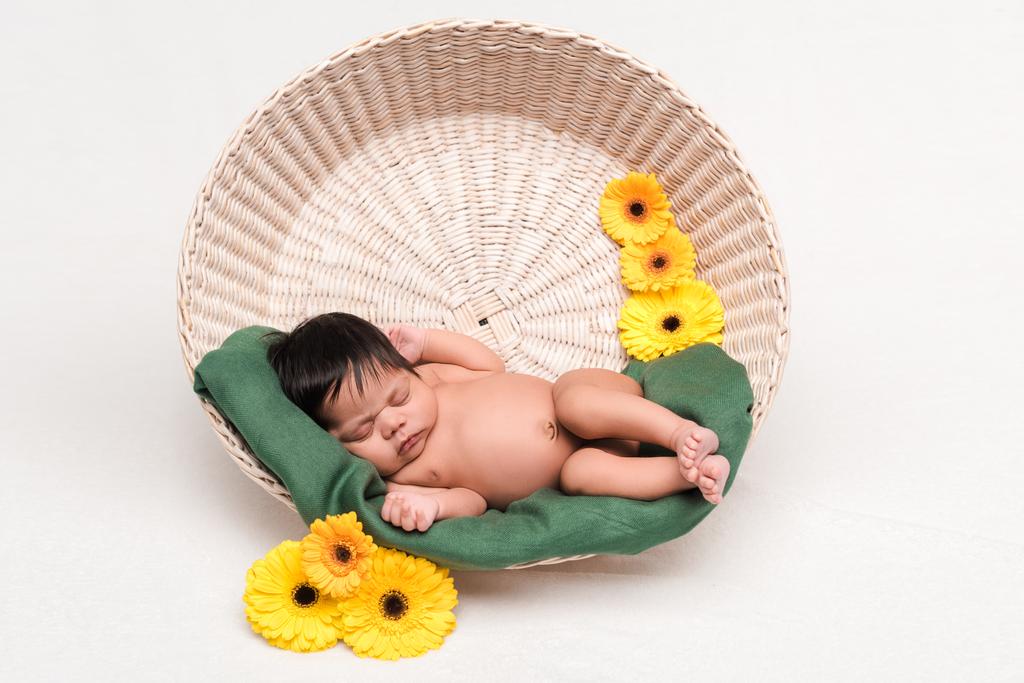 schattig pasgeboren gemengd ras baby slapen in mand in de buurt van bloemen op wit - Foto, afbeelding