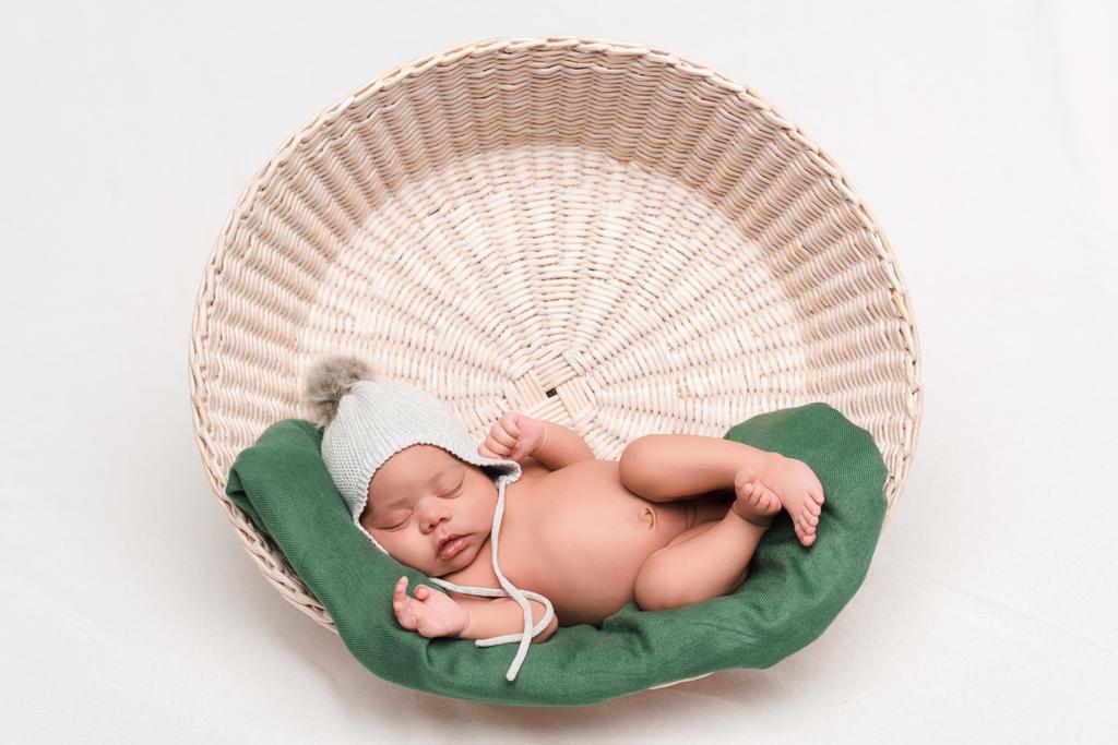 nu recém-nascido misto raça bebê em chapéu de malha dormindo em cesta no branco
 - Foto, Imagem
