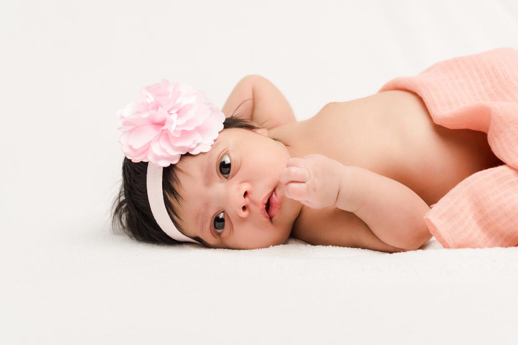 adorable bi-racial newborn baby in headband lying on white  - 写真・画像
