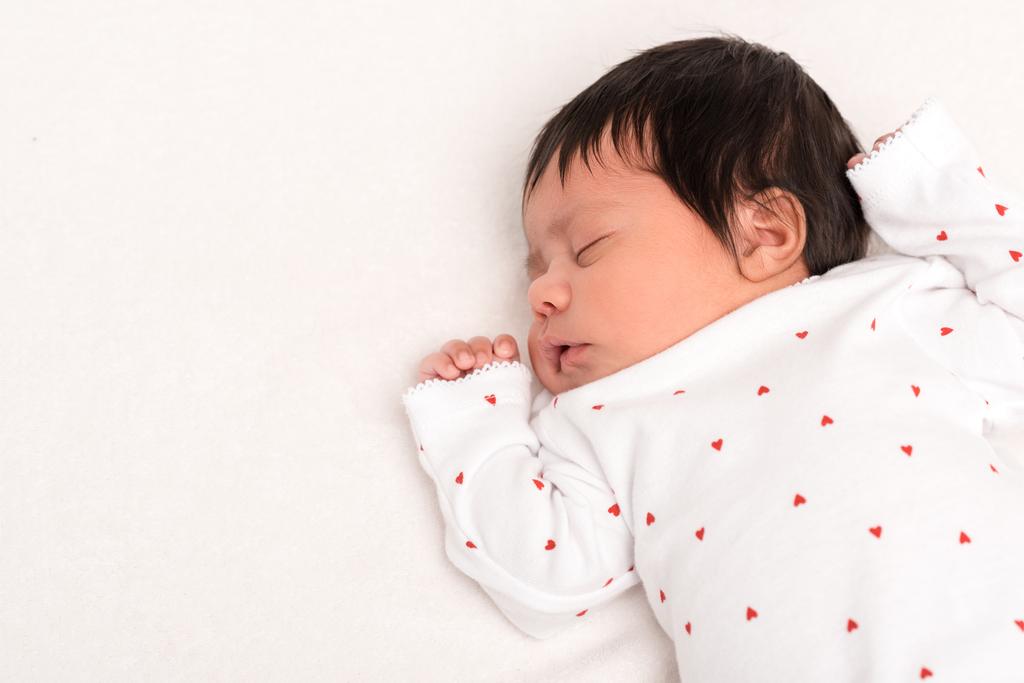 bovenaanzicht van schattige bi-raciale pasgeborene in baby romper slapen geïsoleerd op wit  - Foto, afbeelding