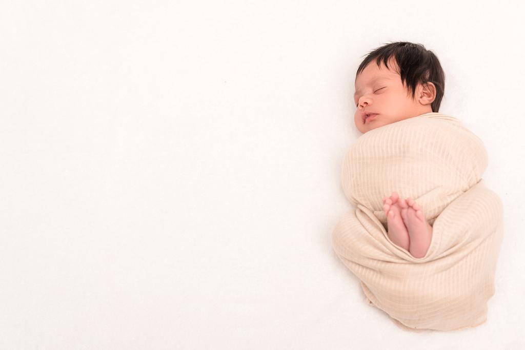 bovenaanzicht van bi-raciale baby verpakt in deken slapen geïsoleerd op wit  - Foto, afbeelding