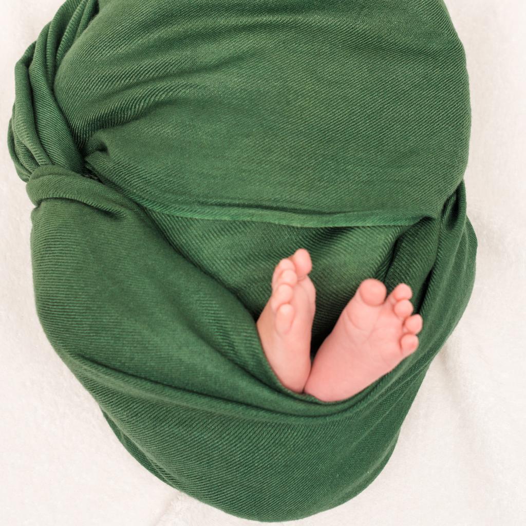 vista cortada do bebê envolto em cobertor verde deitado no branco
  - Foto, Imagem