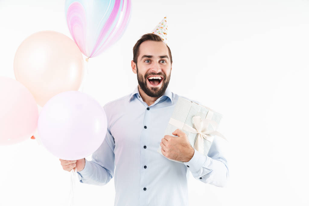 Imagen del hombre de la fiesta feliz sonriendo mientras sostiene globos de aire y caja presente aislado sobre fondo blanco
 - Foto, Imagen