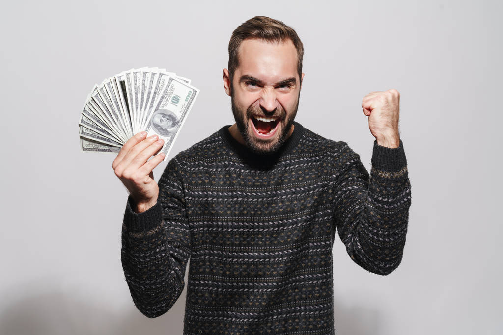Изображение успешного брюнетки мужчина кричит и держа доллар ба
 - Фото, изображение