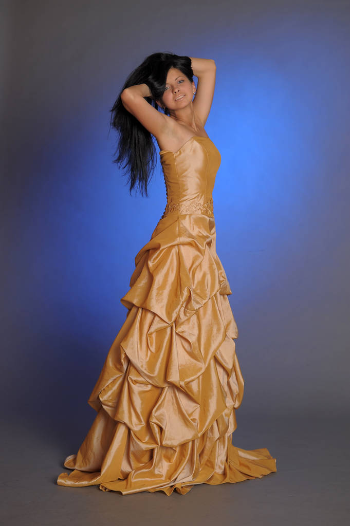 μελαχρινή κοπέλα σε ένα μακρύ χρυσό φόρεμα στο στούντιο - Φωτογραφία, εικόνα
