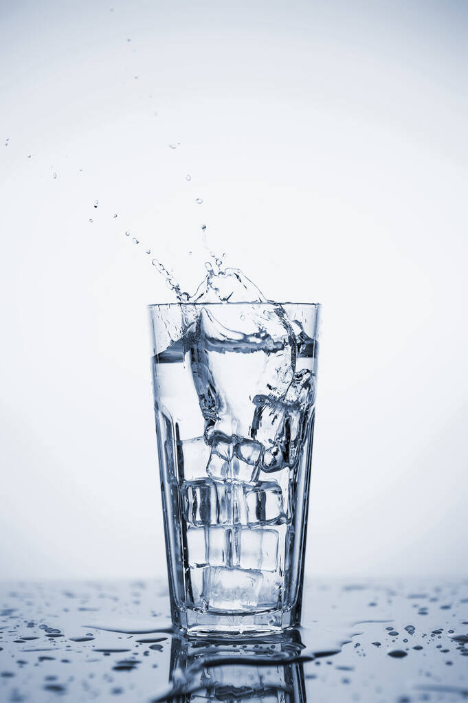 Klares Mineralwasser spritzt in ein Glas mit Eis. - Foto, Bild