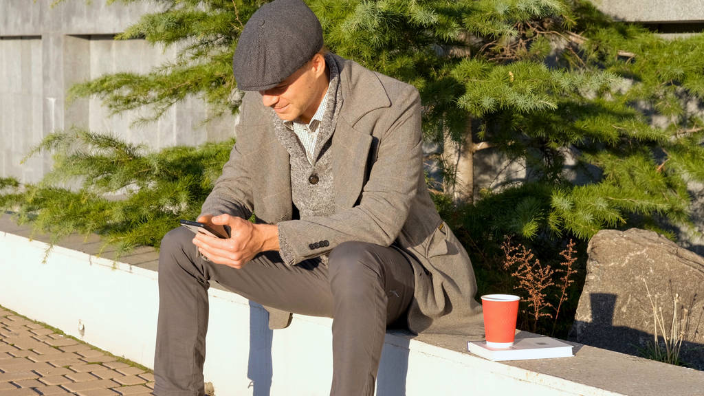 Молодий стильний чоловік з мобільним телефоном і кавою в парку
 - Фото, зображення