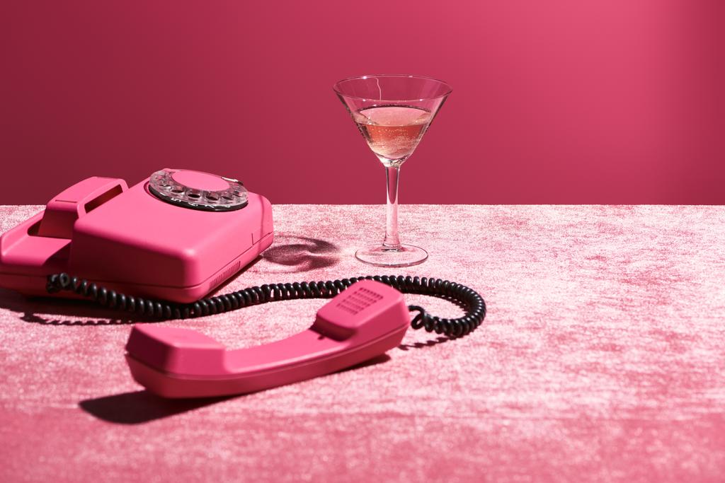 rose wijn in glas in de buurt van vintage telefoon op velours roze doek geïsoleerd op roze, meisjesachtige concept - Foto, afbeelding