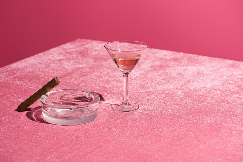 τριαντάφυλλο κρασί σε ποτήρι κοντά πούρο στο τασάκι σε βελούδινο ροζ πανί απομονωμένο σε ροζ, κοριτσίστικη έννοια - Φωτογραφία, εικόνα
