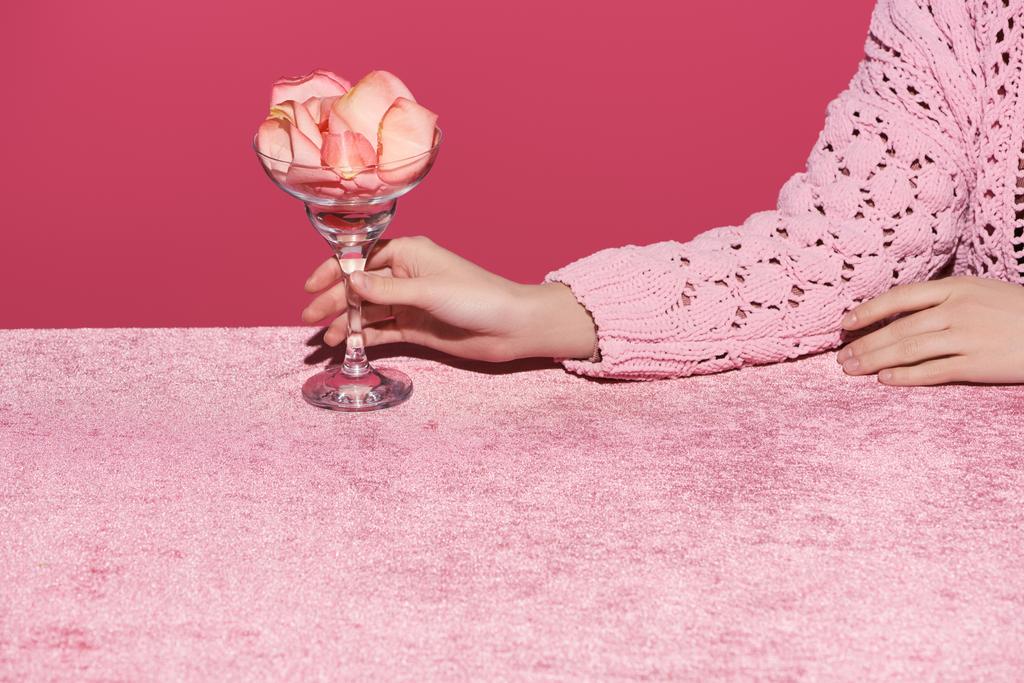обрезанный вид женщины, держащей стекло с лепестками роз на велюровой ткани, изолированной на розовой, девичьей концепции
  - Фото, изображение