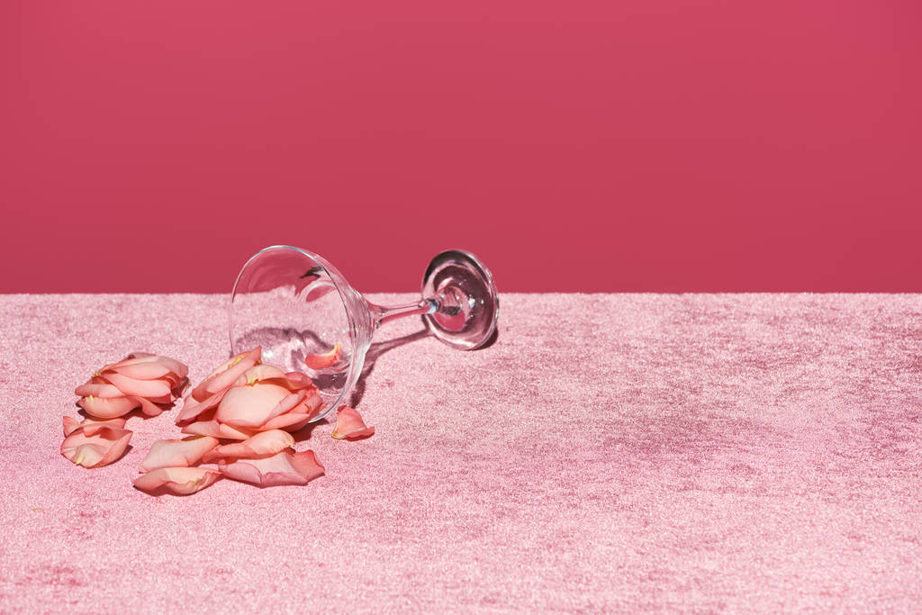 płatki róży w pobliżu szkła na welurowym różowym materiale wyizolowane na różowym, dziewczęcym koncepcie - Zdjęcie, obraz