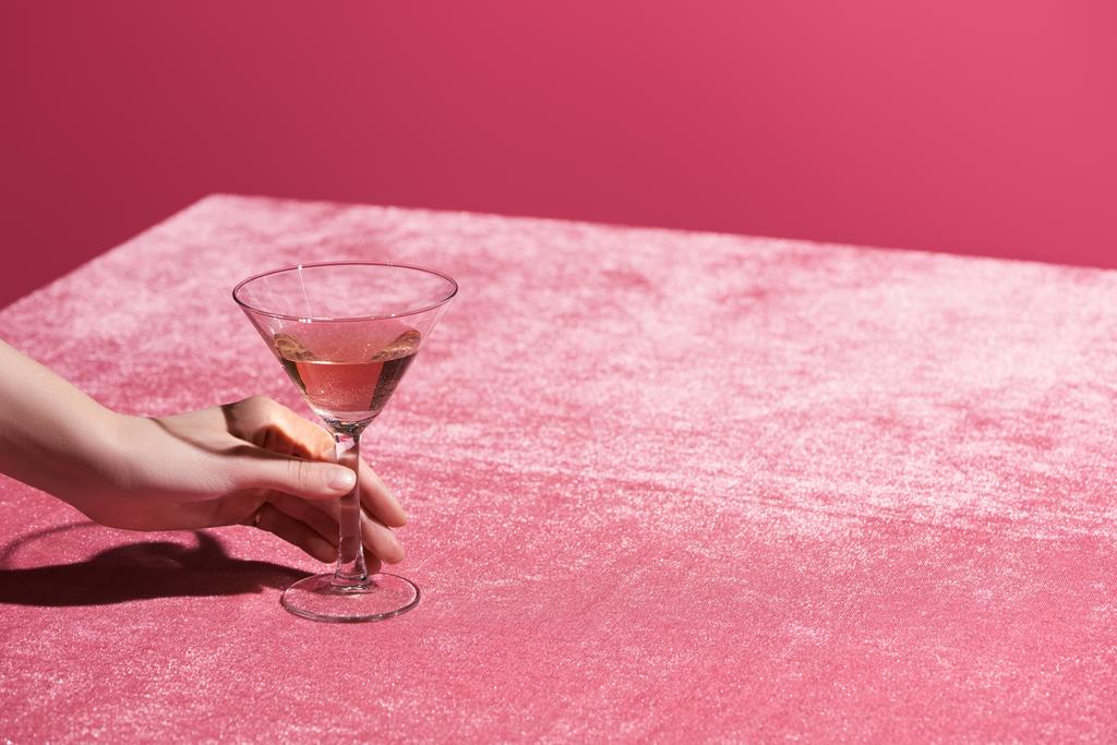 καλλιεργημένη άποψη της γυναίκας κρατώντας ένα ποτήρι ροζέ κρασί σε βελούδινο ύφασμα που απομονώνεται σε ροζ, κοριτσίστικη έννοια  - Φωτογραφία, εικόνα
