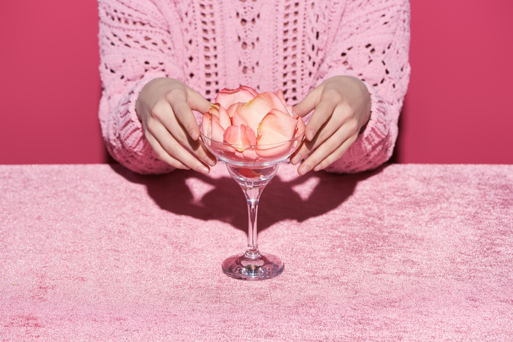 καλλιεργημένη άποψη της γυναίκας με πέταλα σε γυαλί σε βελούδινο ύφασμα που απομονώνονται σε ροζ, κοριτσίστικη έννοια  - Φωτογραφία, εικόνα