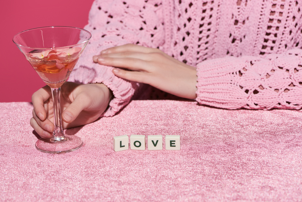 oříznutý pohled ženy držící sklenici růžového vína v blízkosti kostek s milostným nápisem na sametovém plátně izolovaném na růžovém, dívčím pojetí  - Fotografie, Obrázek