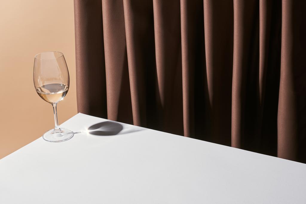 classic still life with glass of white wine on table near curtain isolated on beige - Photo, Image
