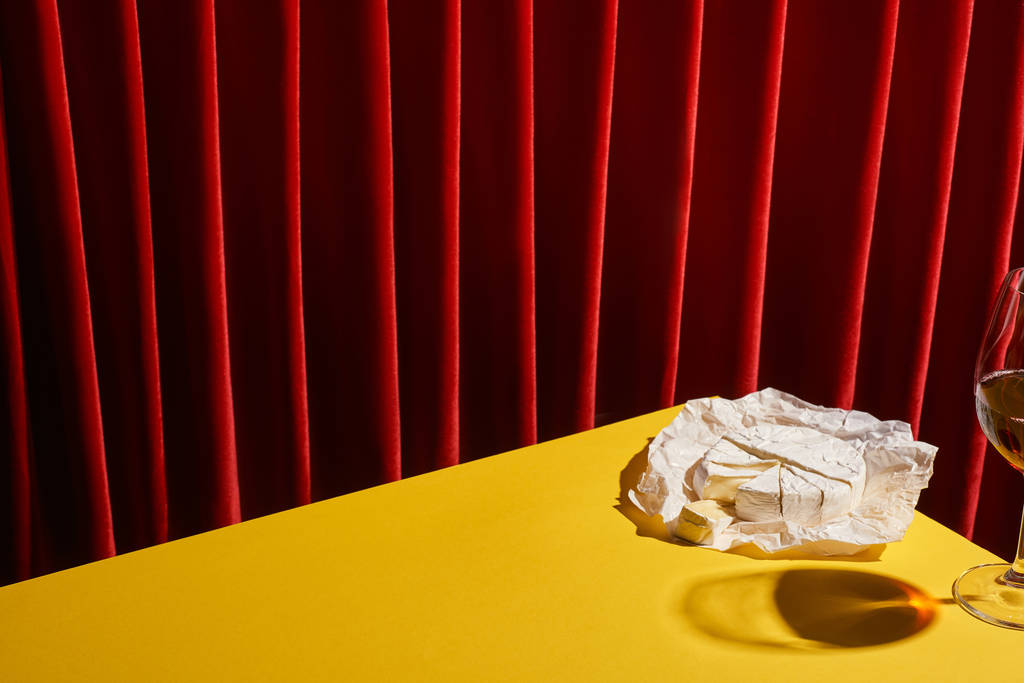 klasický zátiší s Camembert v blízkosti skla červeného vína na žlutém stole v blízkosti červené opony - Fotografie, Obrázek