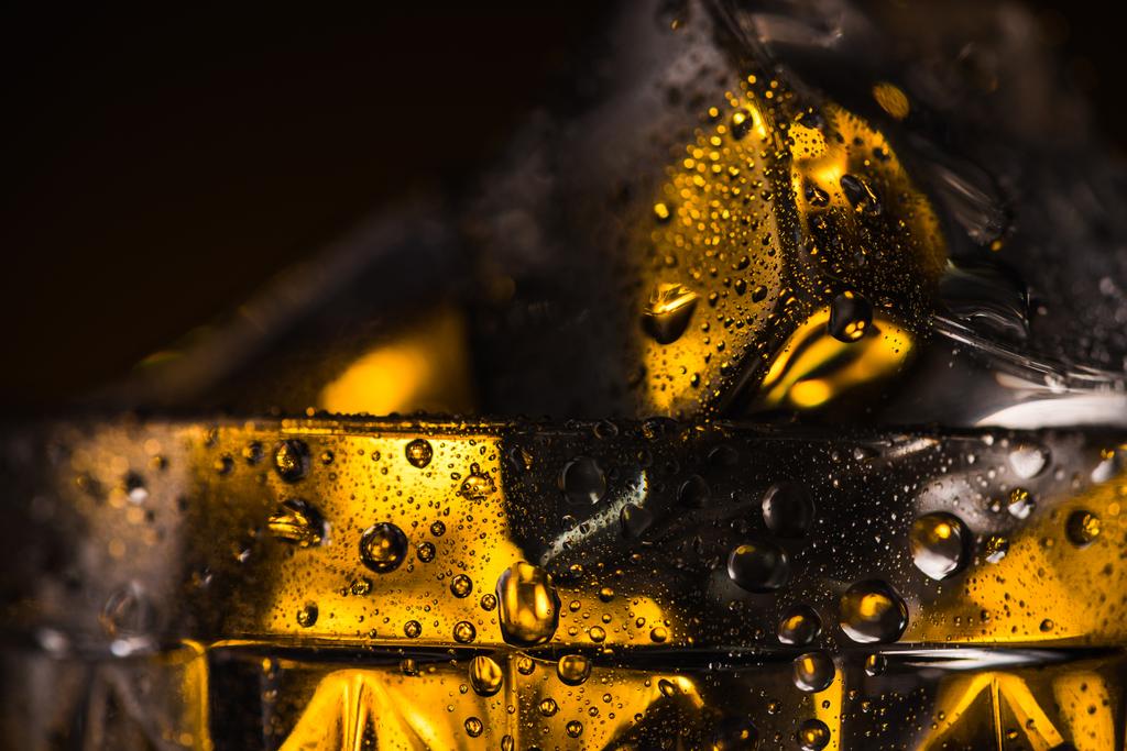 close-up zicht op vierkante ijsblokje in nat geslepen glas met gele verlichting - Foto, afbeelding