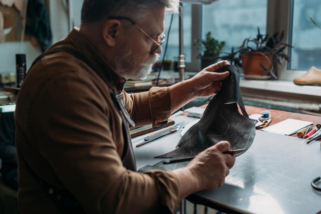 старший сапожник держит куски натуральной кожи в мастерской
 - Фото, изображение