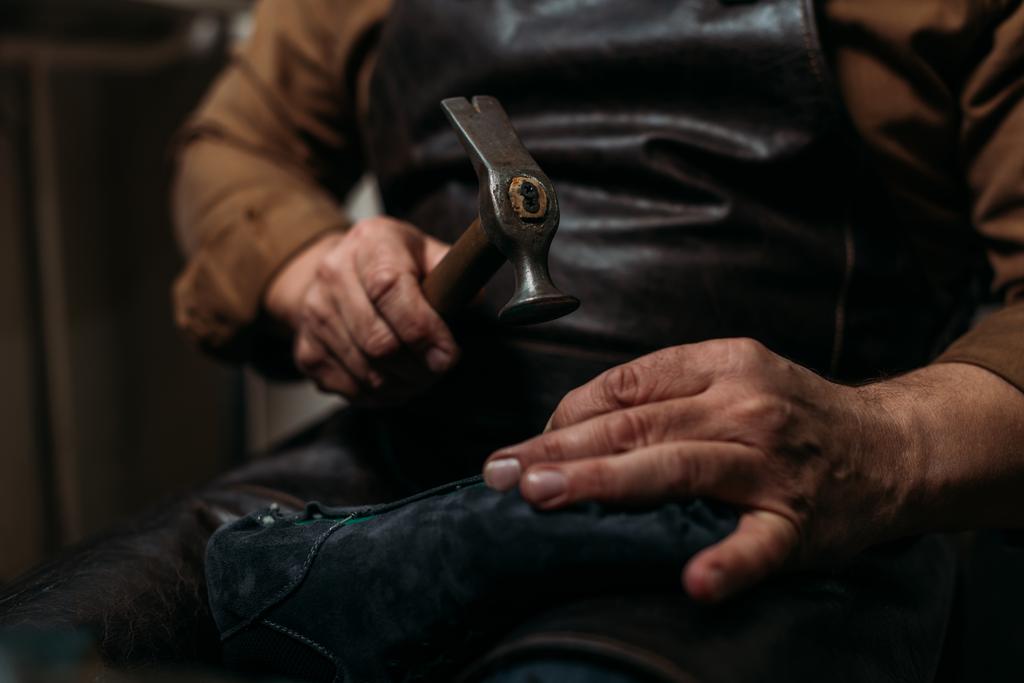 oříznutý pohled na obuvníka držícího hummer při opravě boty v dílně - Fotografie, Obrázek