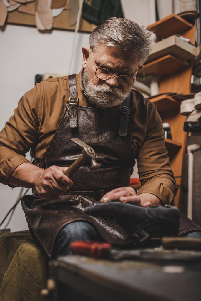 zapatero barbudo senior que sostiene el zapato mientras repara el zapato en el taller
 - Foto, imagen