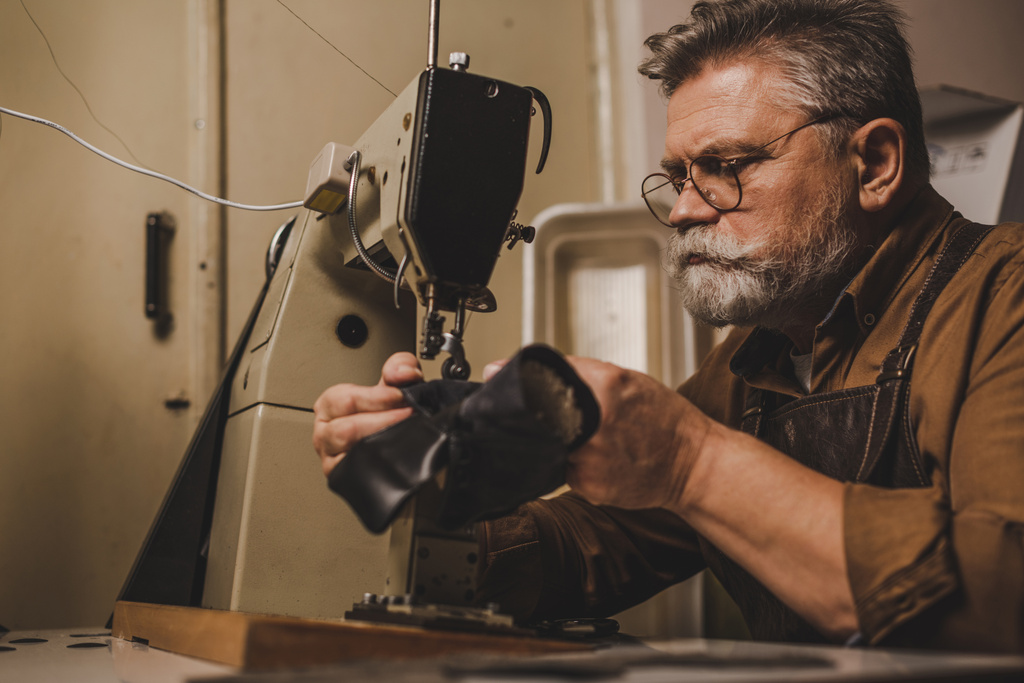 cobbler sênior, barbudo costura parte do sapato de couro na máquina de costura
 - Foto, Imagem