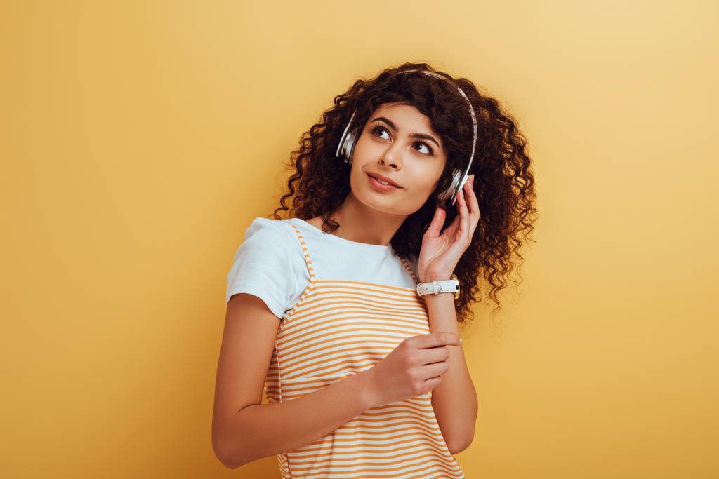 dreamy, positive mixed race girl in wireless headphones looking away on yellow background - Photo, Image