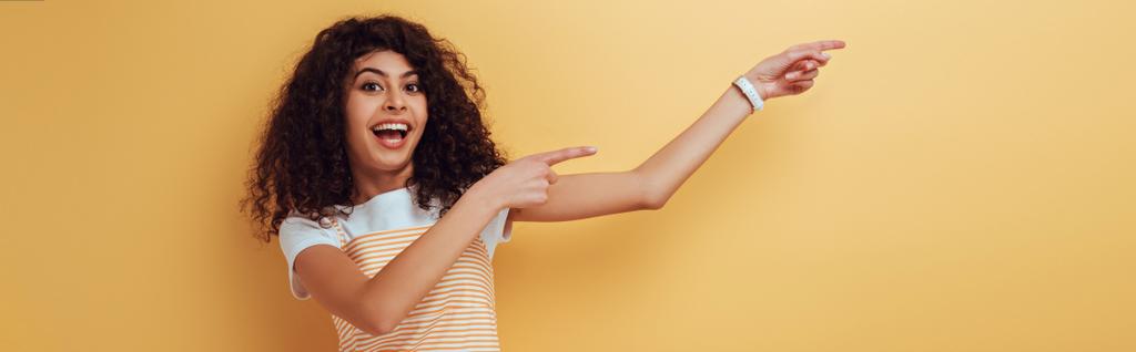 plano panorámico de alegre chica bi-racial señalando con los dedos sobre fondo amarillo
 - Foto, imagen