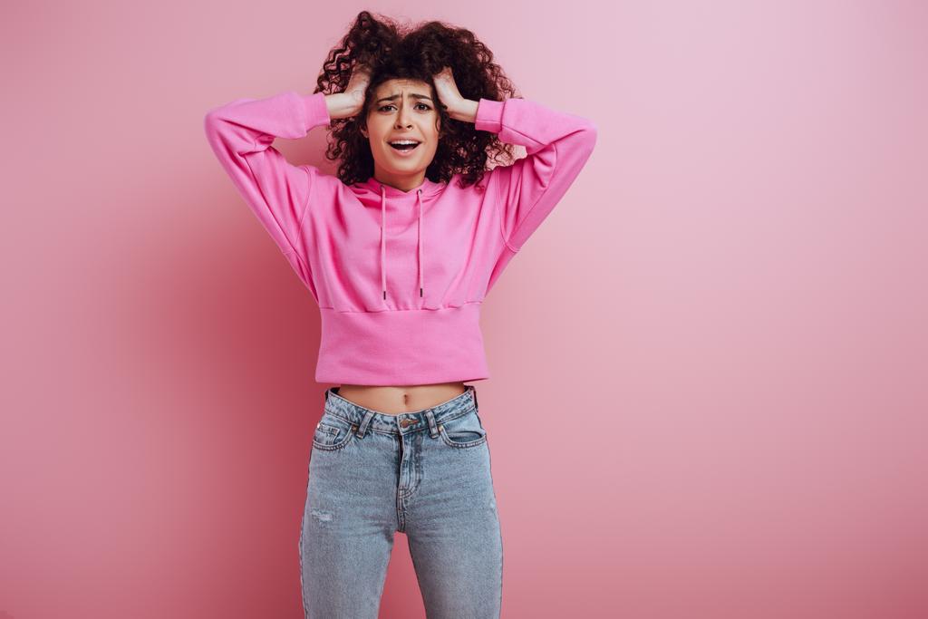 worried bi-racial girl touching head and looking at camera on pink background - Photo, Image