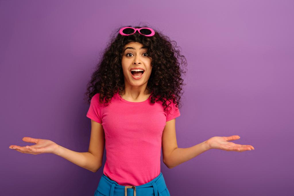 rozczarowana bi-rasowy dziewczyna pokazując wzruszający gest patrząc na aparat fotograficzny na fioletowym tle - Zdjęcie, obraz