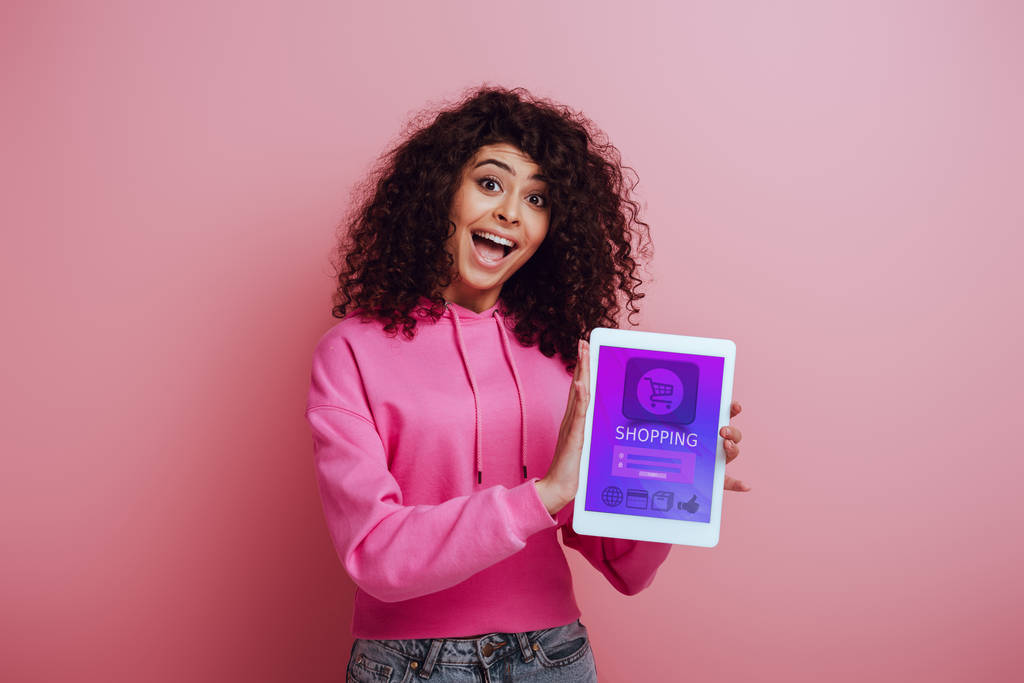 ενθουσιασμένοι bi-φυλετικό κορίτσι δείχνει ψηφιακή tablet με ψώνια app σε ροζ φόντο - Φωτογραφία, εικόνα