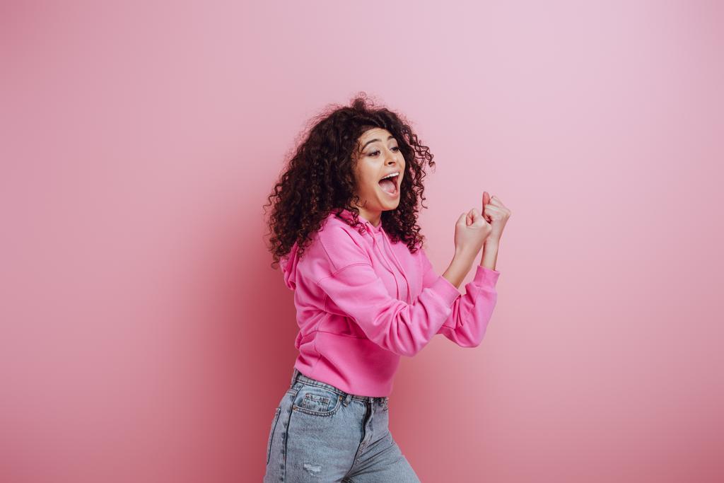 excited bi-racial girl shouting while showing winner gesture on pink background - Photo, Image