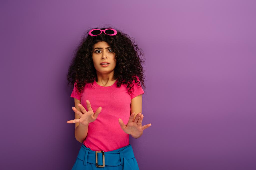scared bi-racial girl showing stop gesture while looking at camera on purple background - Photo, Image
