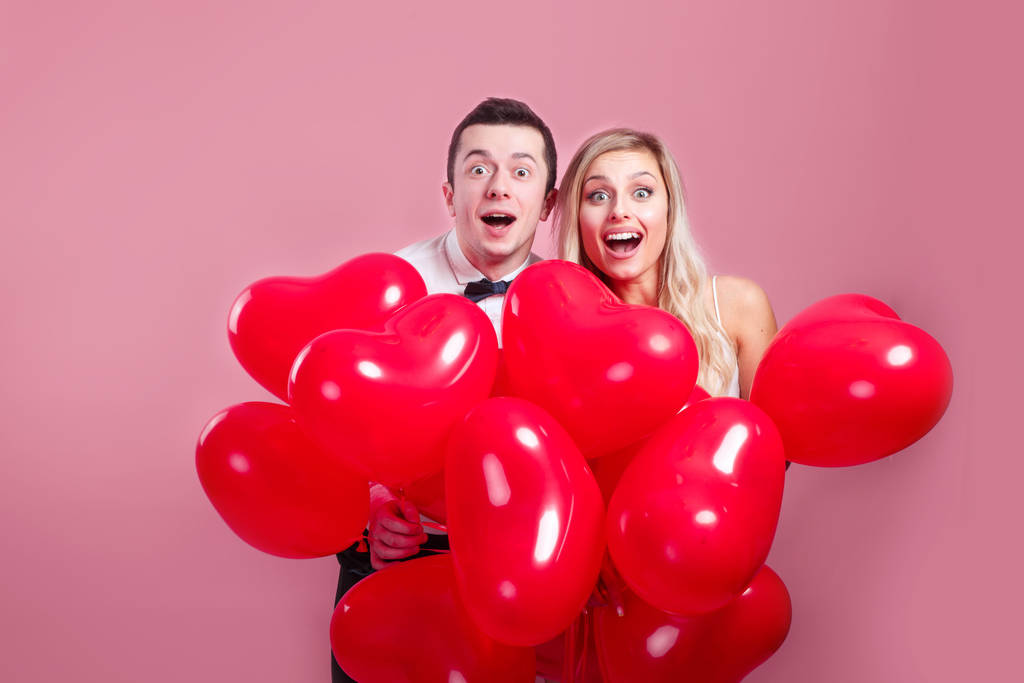 Hauska yllättynyt nuori pari ilmapalloja sydän vaaleanpunainen tausta
 - Valokuva, kuva