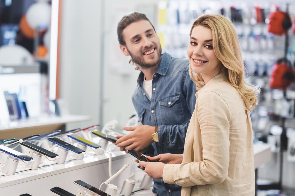 novio y novia sonrientes sosteniendo nuevos teléfonos inteligentes en la tienda de electrodomésticos
  - Foto, Imagen