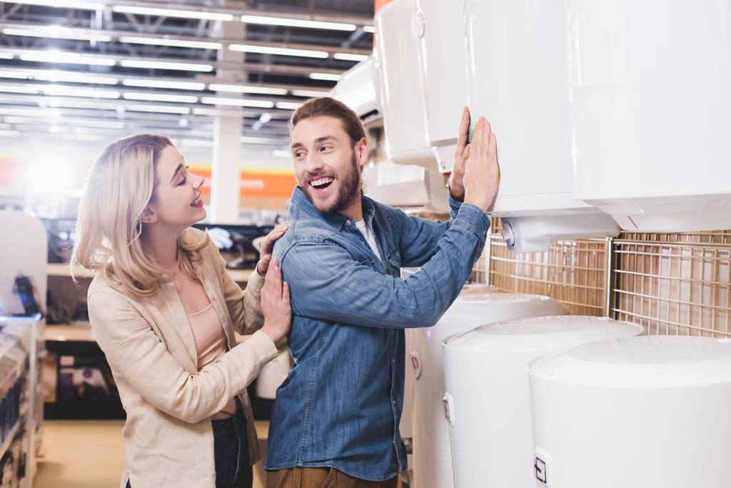 petit ami souriant touchant chaudière et regardant petite amie dans le magasin d'appareils ménagers
  - Photo, image