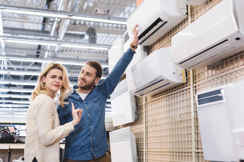 namorado apontando com a mão para ar condicionado e namorada mostrando nenhum gesto na loja de eletrodomésticos
  - Foto, Imagem