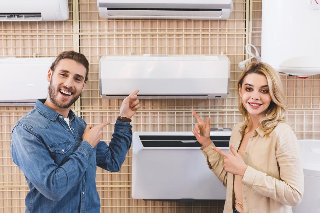 mosolygós barát és barátnő ujjal mutogat a légkondicionáló otthoni készülék boltban  - Fotó, kép
